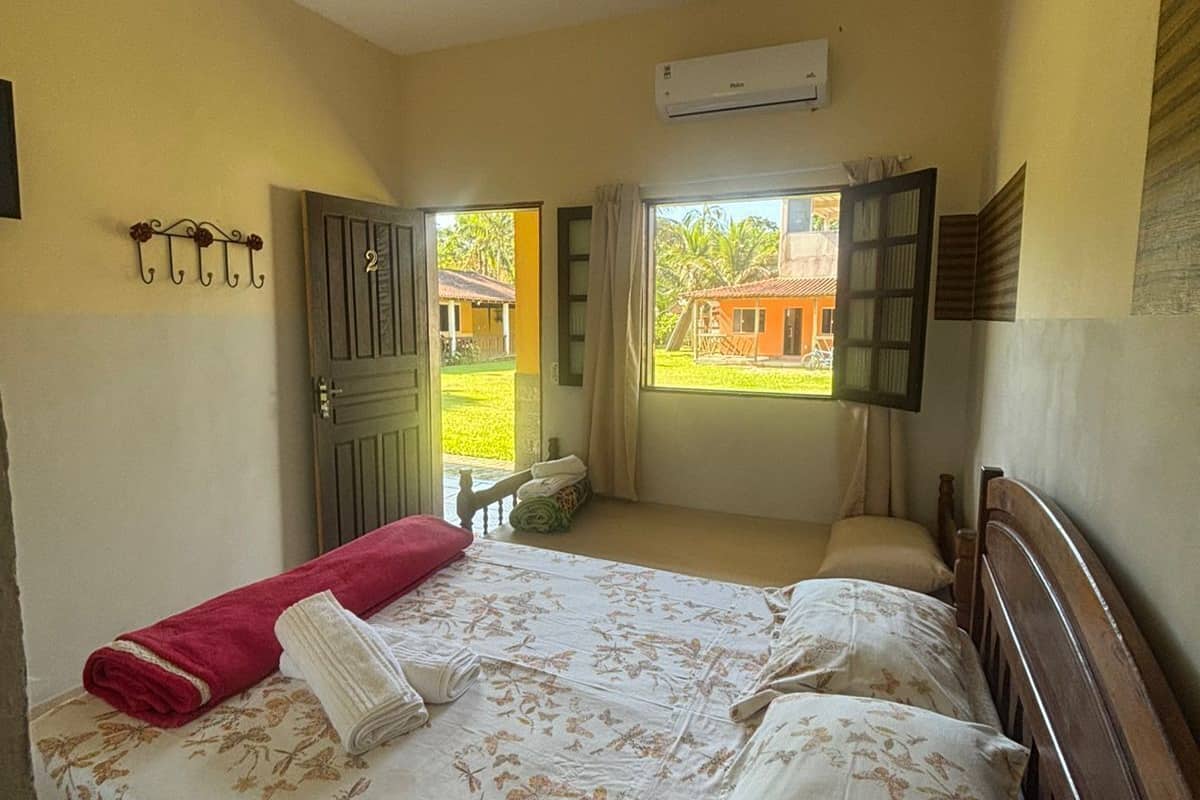 A bedroom with a bed, a window, an air conditioning unit, and a door leading outside.