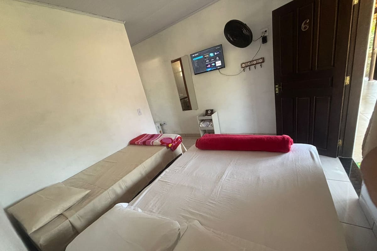 A room with two beds, a wall-mounted TV, a fan, and a door with a number.
