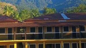A two-story building with a tiled roof, multiple windows, and a car parked in front. - Pousada cachoeira  (Paraty)