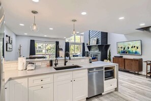 A modern kitchen with white cabinetry, a stainless steel dishwasher, pendant lighting, and a large window. - Stop in for the Ultimate Mountain Lifestyle! (Frisco)