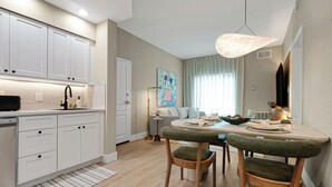 Eine moderne Küche mit weißen Schränken, ein Essbereich mit einem runden Tisch und ein großes Fenster mit Vorhängen.