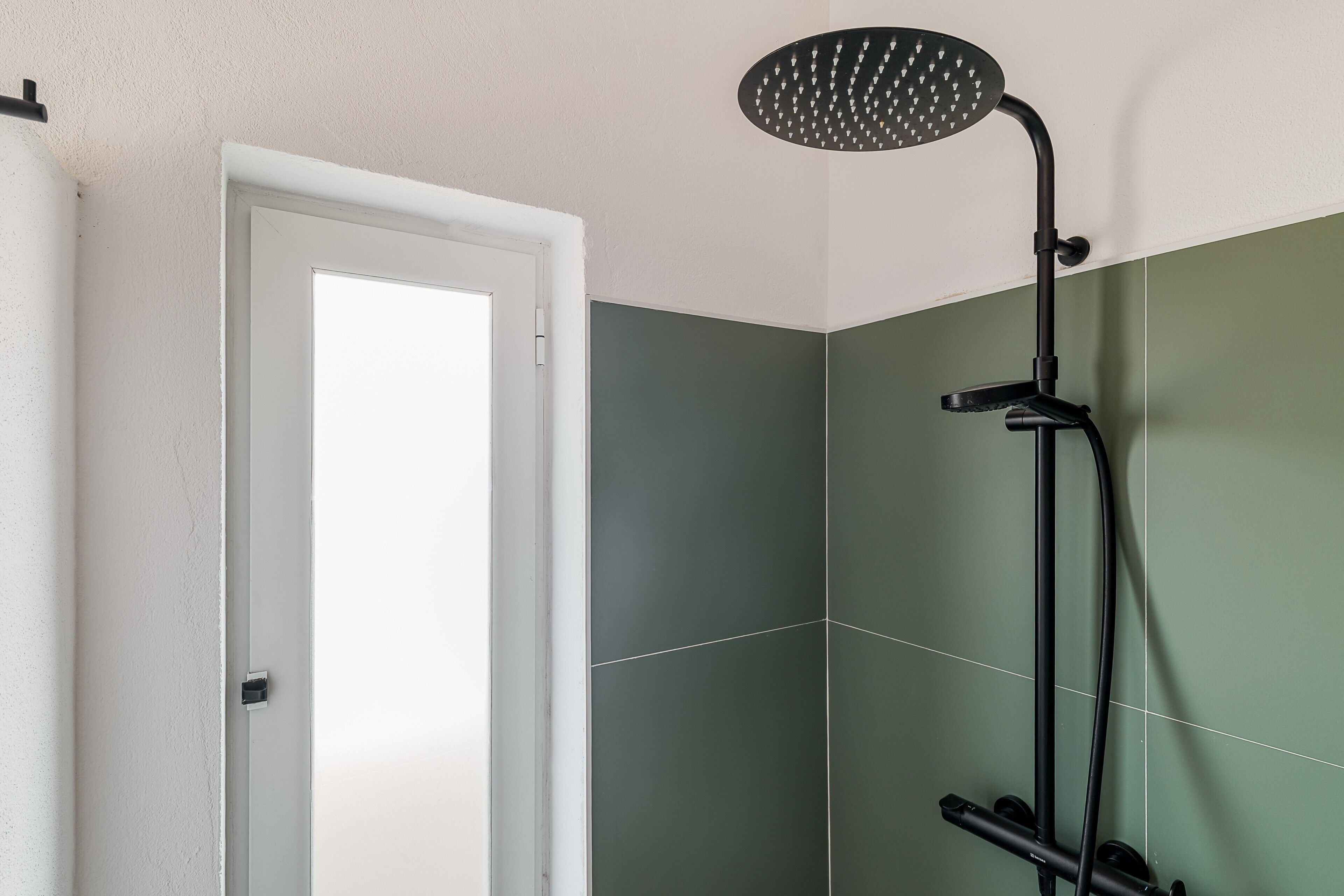Un bagno con doccia, una porta e pareti verdi e bianche.