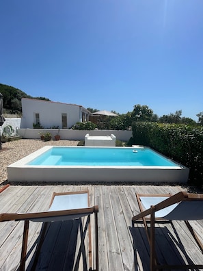 A rectangular swimming pool with a wooden deck in the foreground, a white building in the background, and a clear blue sky. - Studio Apartment 'Studiolive At Marina Vale Figueira' with Shared Pool, Wi-Fi and Air Conditioning (Melides)