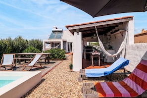 An outdoor patio with a pool, lounge chairs, a hammock, and a covered seating area.