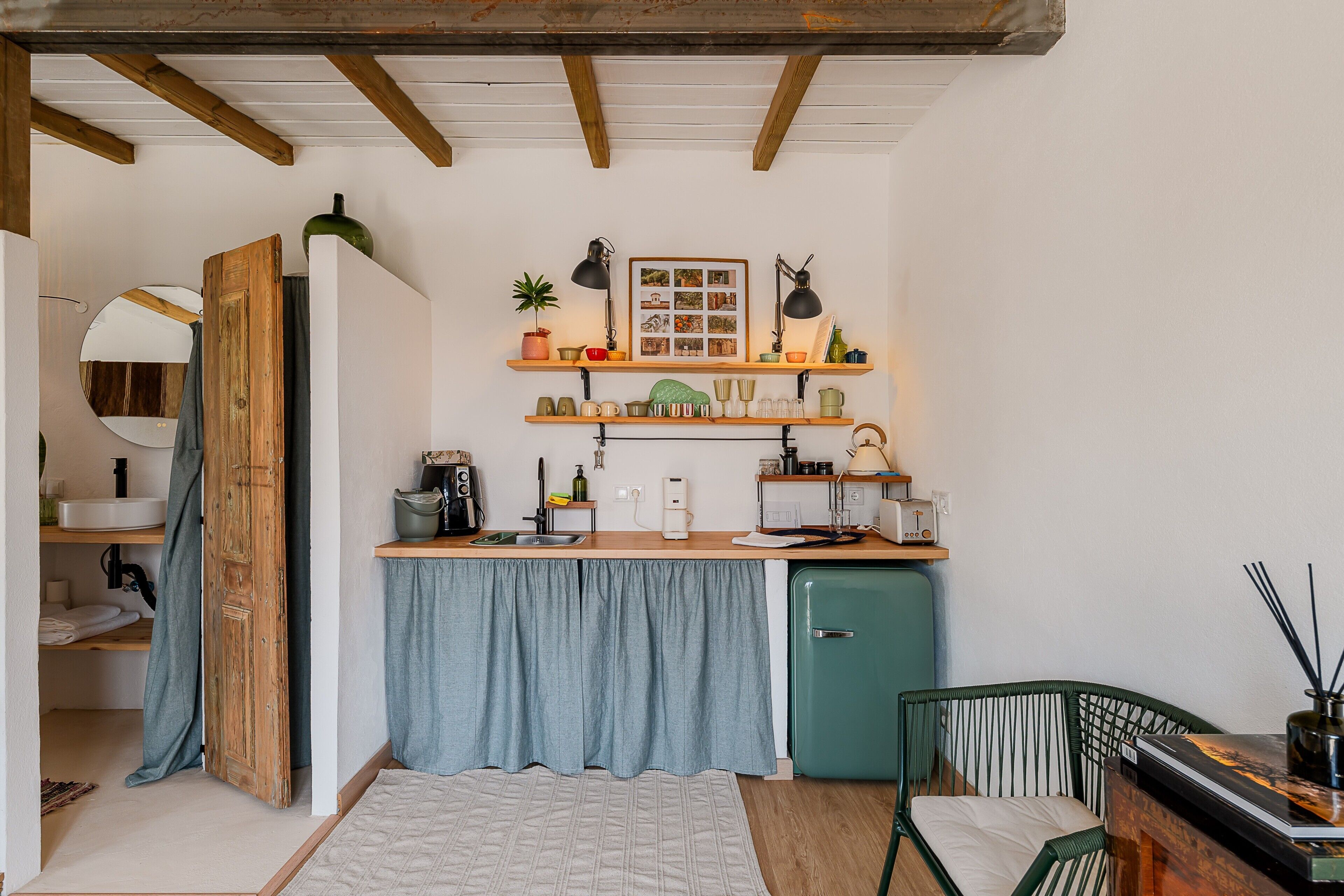 A compact kitchen with a built-in fridge, wooden shelves, and a small dining area with a chair.