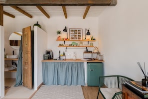 A compact kitchen with a built-in fridge, wooden shelves, and a small dining area with a chair.