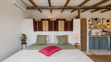 A bedroom with a bed, a nightstand, a lamp, a potted plant, and a wooden ceiling.