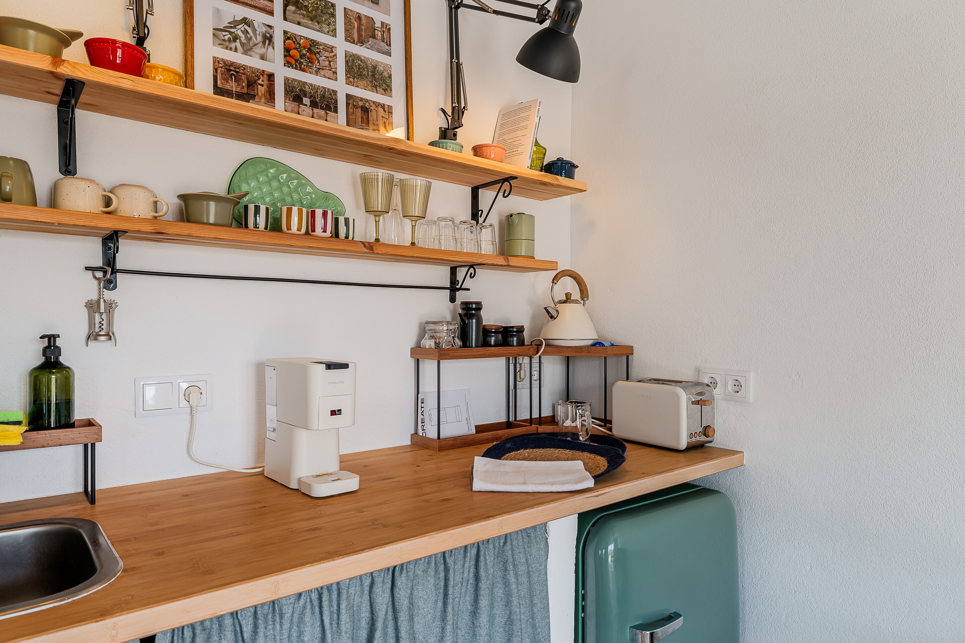 A kitchen with wooden shelves, a coffee maker, a kettle, and a toaster.