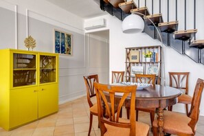Ein Essbereich mit einem gelben Schrank, Holzkästen, einem runden Tisch und einer Treppe mit Pendelleuchte.