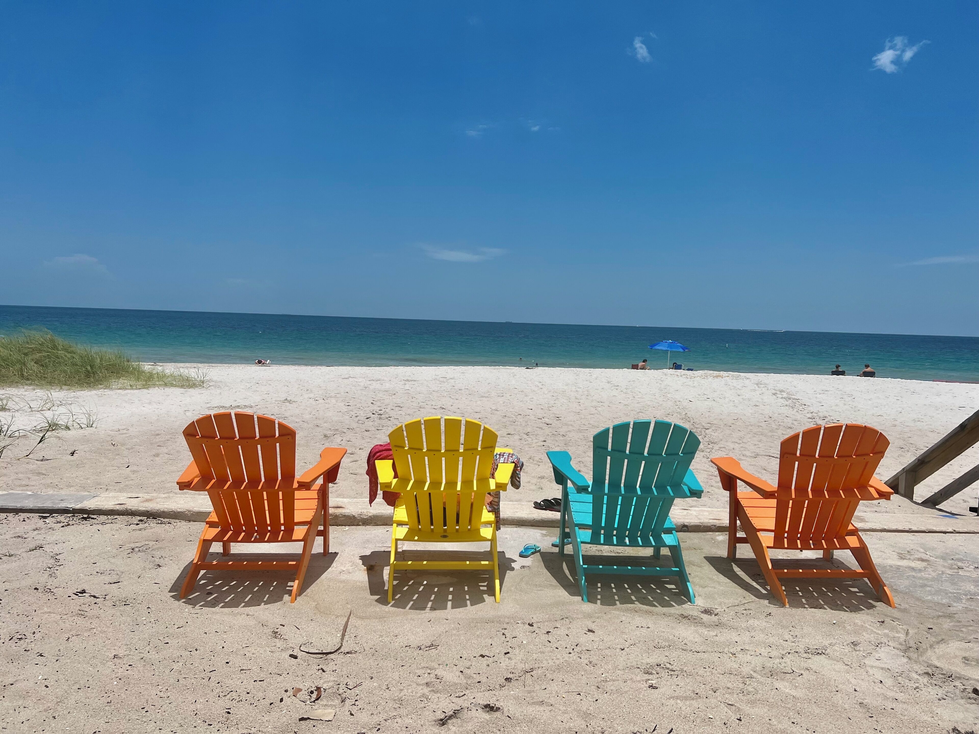 A beach with four colorful Adirondack chairs facing the ocean.