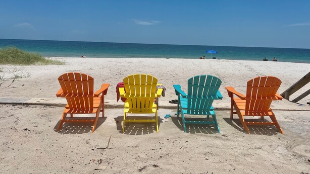 Una spiaggia con quattro poltrone Adirondack colorate rivolte verso l'oceano.