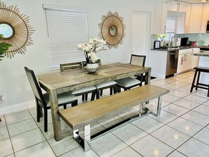A dining area with a wooden table, chairs, and a bench. There are decorative wall mirrors and a potted plant with white flowers. - 
The perfect getaway ,ONLY 2 Minutes away from  the beach!!!! (Fort Lauderdale)