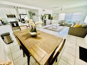 A modern kitchen with white cabinets, a microwave, and a dining area with a wooden table and chairs. - 
The perfect getaway ,ONLY 2 Minutes away from  the beach!!!! (Fort Lauderdale)