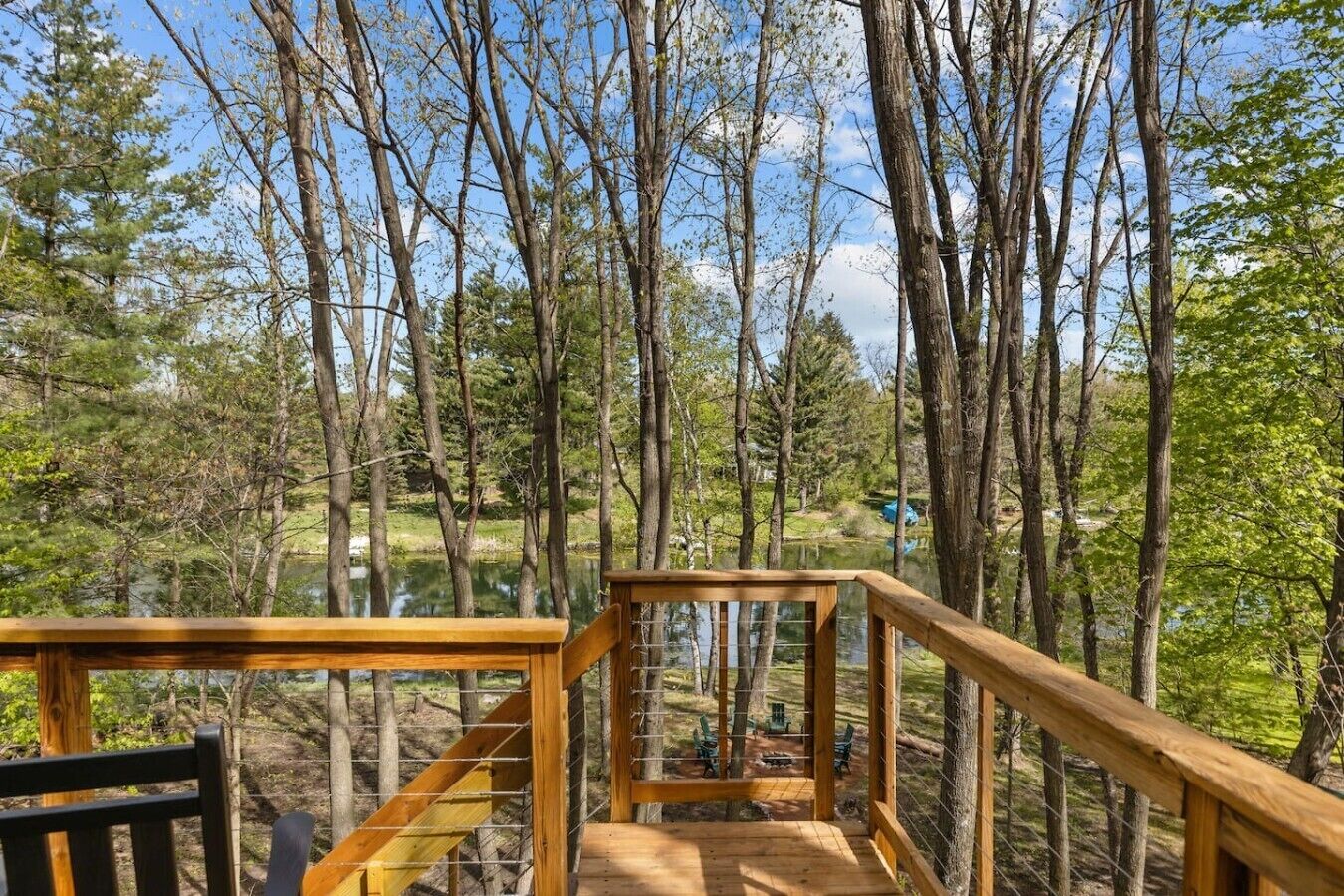 Une terrasse en bois dotée d’une rambarde, qui offre une vue sur une zone boisée et un plan d’eau.