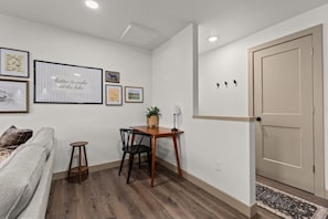 Ein Zimmer mit Holzboden, einer Couch, einem Esstisch mit Stühlen, einem kleinen Beistelltisch mit Lampe und einer Tür.