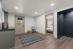 Ein Zimmer mit Tür, einem Sessel, einem Bett und einer dunklen Wand.