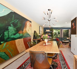 A dining area with a large painting, a chandelier, and a view of greenery outside.