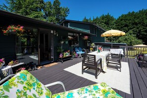 A deck with outdoor furniture, a table with a tablecloth, and hanging flower baskets.