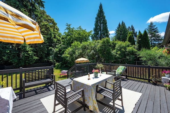 A wooden deck with a table and chairs, surrounded by a wooden fence and lush greenery.
