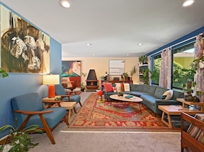 A living room with a blue sofa, a coffee table, a fireplace, and a large window with curtains.