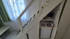 Eine Treppe führt zu einer Küchenzeile mit Kühlschrank, Kochgeschirr und einem Fenster mit Vorhängen.