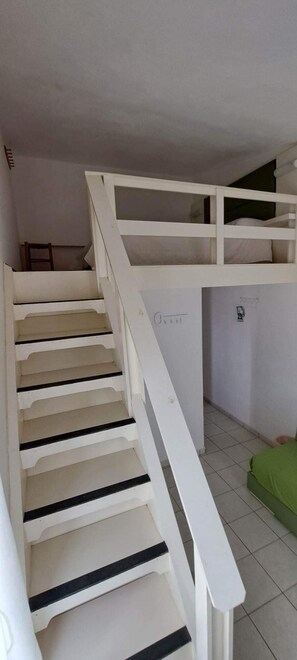 Eine Treppe mit weißen Geländern und beigen Stufen führt zu einer Erkerzone mit einem grünen Bett.
