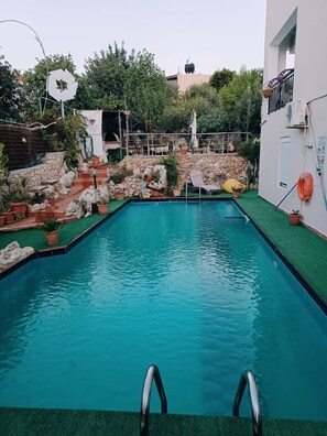 Ein Schwimmbecken mit einer Steinmauer und Stufen zu einem überdachten Bereich.