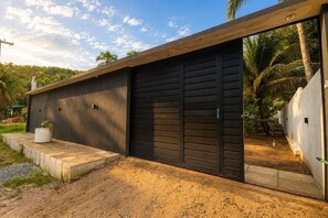 A modern building with a large black garage door, a concrete pathway, and a small potted plant. - Casa com piscina pertinho da Praia do Boqueirão (Japaratinga)