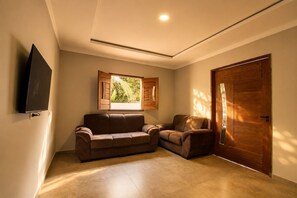 A room with a brown leather sofa, a wooden door, and a window with wooden shutters. - Casa com piscina pertinho da Praia do Boqueirão (Japaratinga)