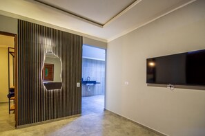 A modern hotel room with a large TV, a sliding door leading to a bathroom, and a view of the outside. - Casa com piscina pertinho da Praia do Boqueirão (Japaratinga)