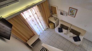 Habitación con sofá, una mesita, televisor montado en la pared y ventana con cortinas.