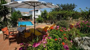 Un área de piscina con sillas y una sombrilla, rodeada de follaje y flores.