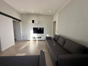 Una sala de estar moderna con un sofá grande de color gris, un televisor de pantalla plana montado en la pared y un mueble blanco para equipos electrónicos.
