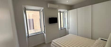 Une chambre à coucher avec un lit, deux fenêtres, un climatiseur et un téléviseur fixé au mur.