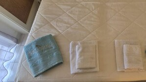 Una cama con un colchón blanco acolchado, dos toallas dobladas y una toalla azul al lado.