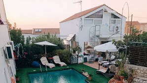 Una piscina rectangular con una pequeña cascada, rodeada de césped artificial y plantas en macetas.