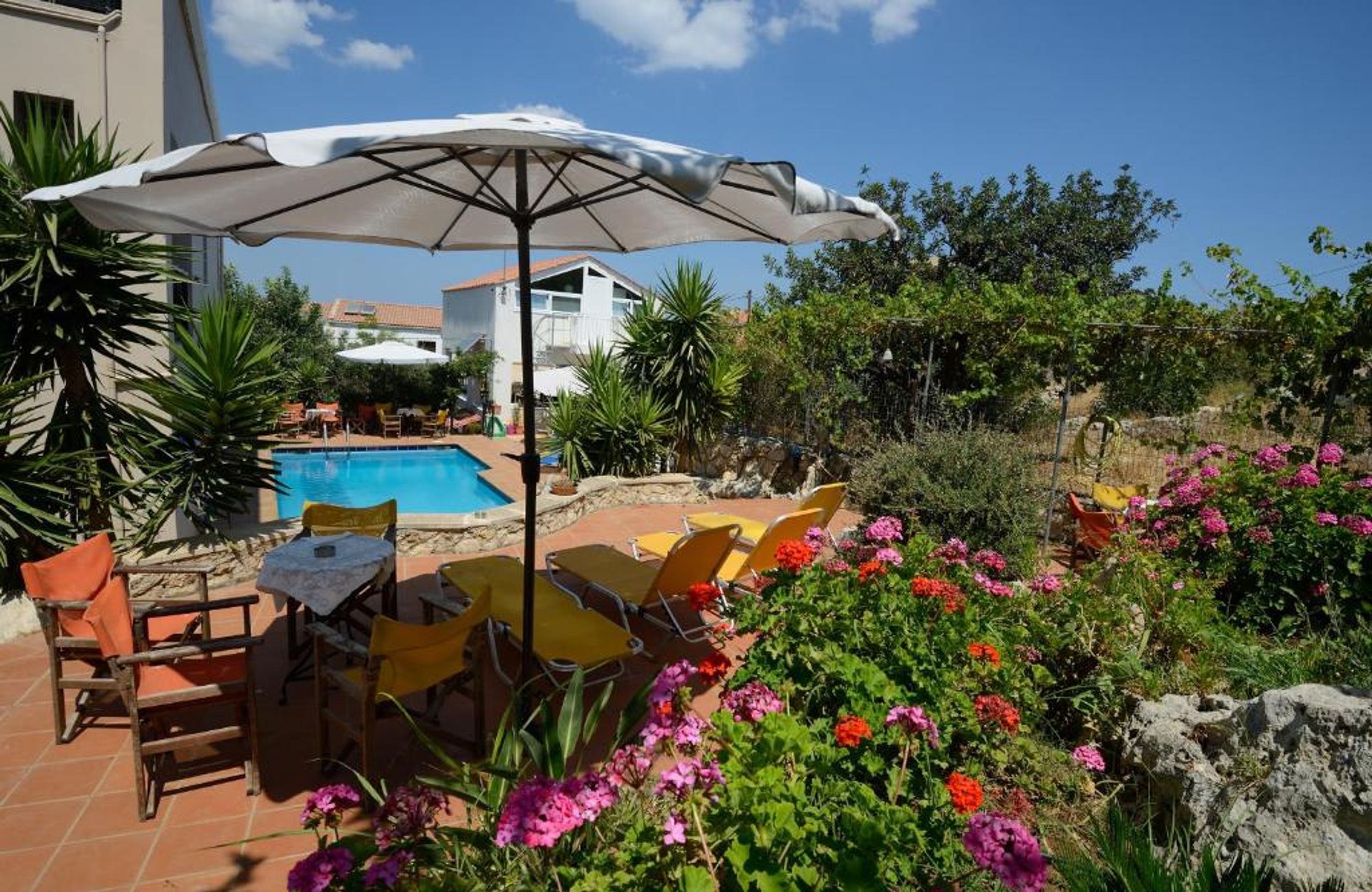 A pool area with chairs and an umbrella, surrounded by greenery and flowers.