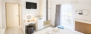 A hotel room with a bed, a desk with a mirror, a television, a window with curtains, and a radiator. - Bicorna Chania Pool Escape - Silver Room 3 (Apokoronas)