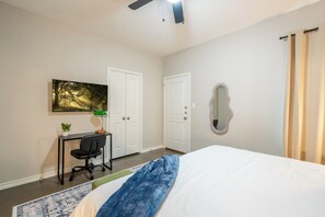 A bedroom with a bed, a desk with a chair, a desk lamp, a potted plant, and a painting on the wall. - 3-bedroom Townhome with High Speed WIFI (Bullard)