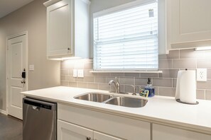 A kitchen with a dishwasher, double sink, and window with blinds. - 3-bedroom Townhome with High Speed WIFI (Bullard)
