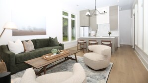A modern living room with a sofa, coffee table, and chairs, a kitchen with a dining area, and large windows.