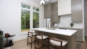 A modern kitchen with a large island, bar stools, and a view of greenery outside.