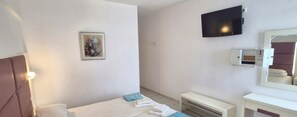 Ein Hotelzimmer mit einem Bett, einem an der Wand montierten Fernseher, einem Spiegel über dem Schminktisch und einem gerahmten Bild an der Wand.