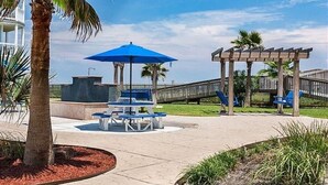 A beachside patio with a blue umbrella, seating, and a wooden pergola.