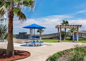 A beachside patio with a blue umbrella, seating, and a wooden pergola.
