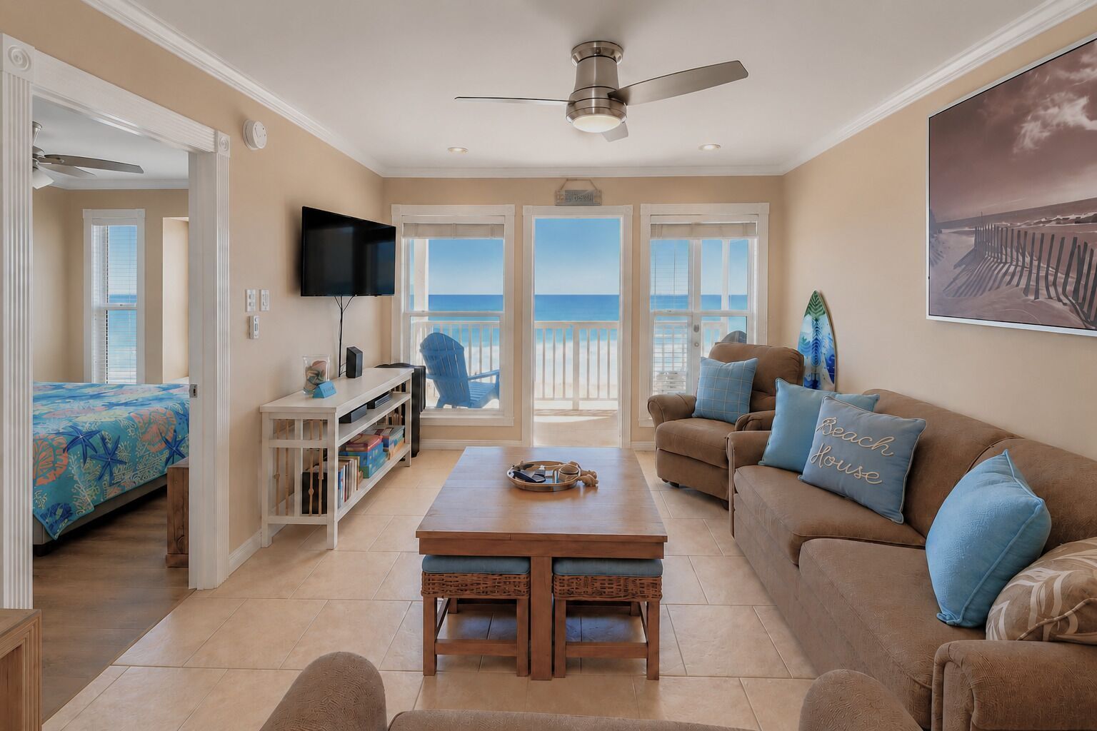 A living room with a TV, a coffee table, a sofa, and a view of the beach.