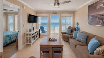 Una sala de estar con televisor, una mesa de centro, un sofá y vista a la playa.