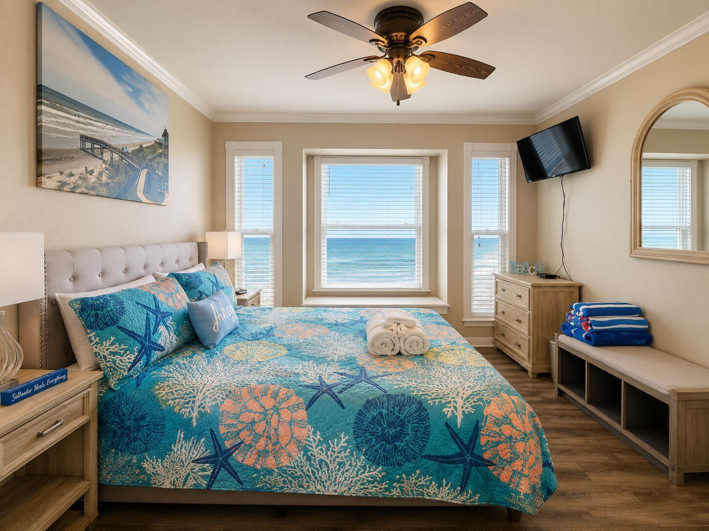 Une chambre à coucher comprenant un lit, un ventilateur de plafond, une télévision, une commode, un banc et un tableau.