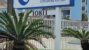 A sign for 'Escape Resort Rental Condominiums' with a white background and blue lettering.