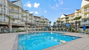 A swimming pool with lounge chairs, a covered area, and a multi-story building with balconies.